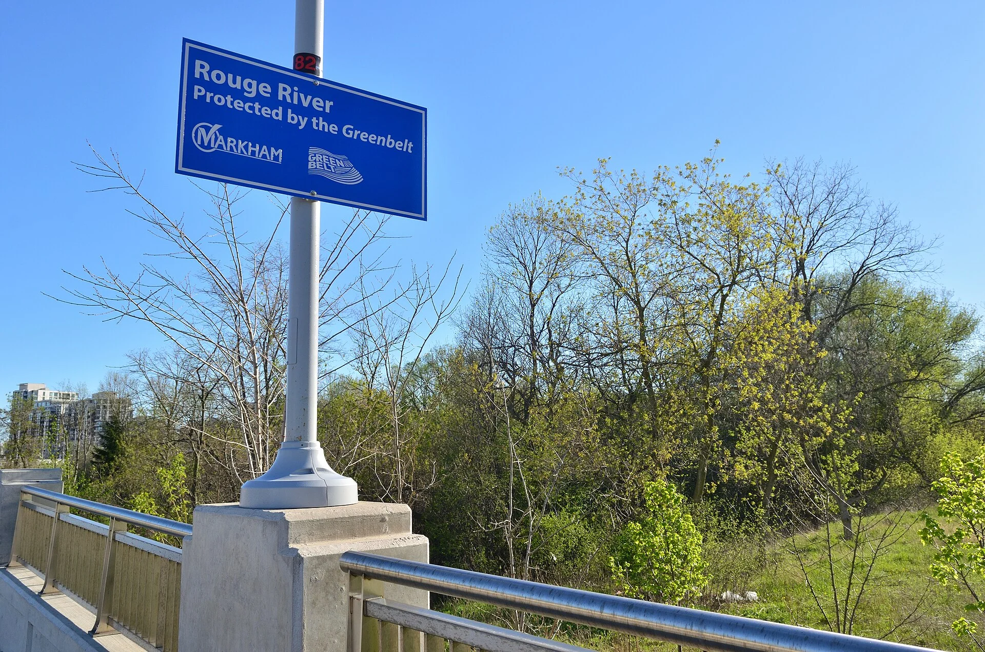 The wooded Rouge River valley seen from a bridge at Birchmount Road and Highway 7 in Markham, beside a sign marking the river as protected by the Greenbelt