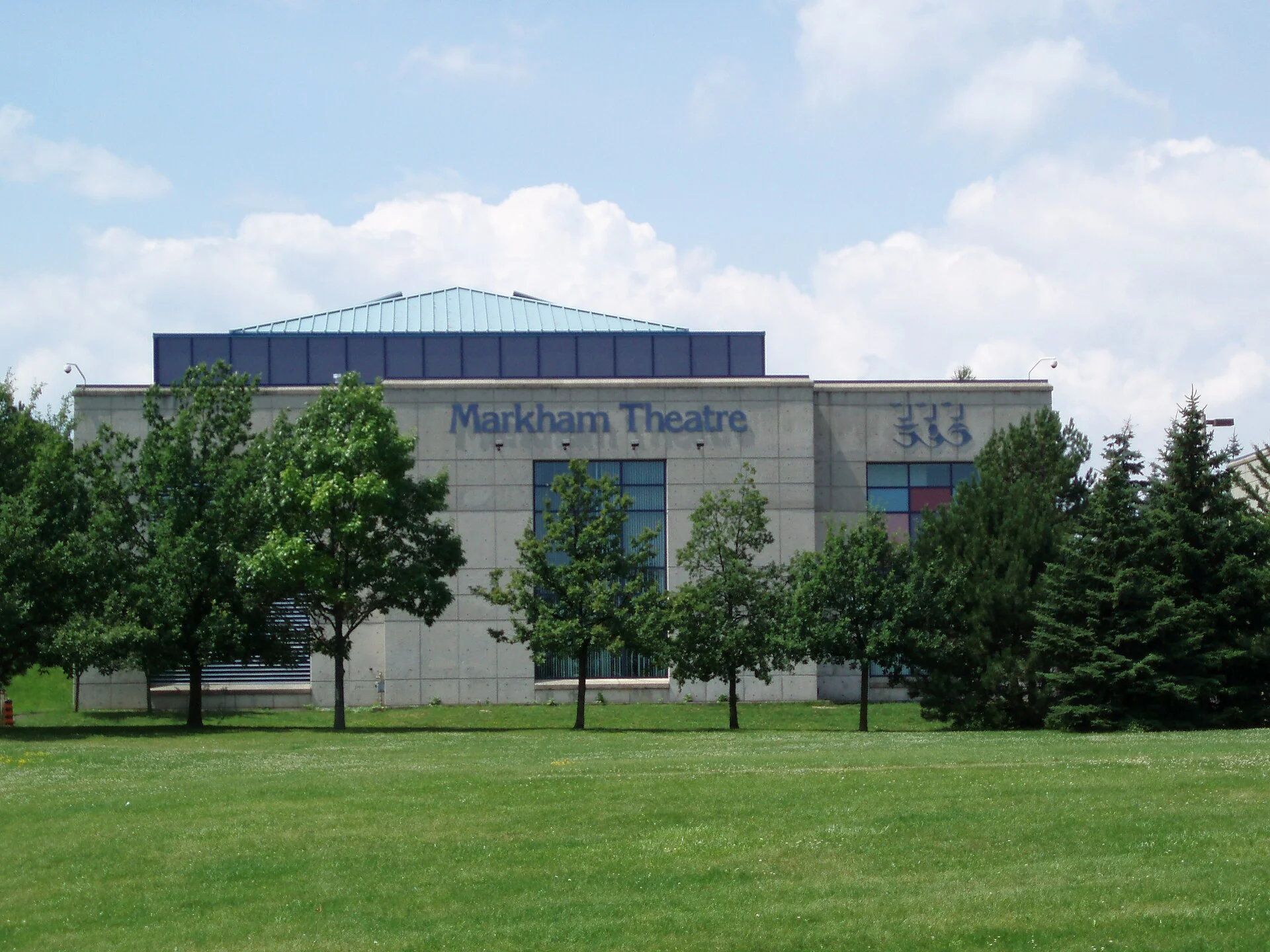 The Markham Theatre building, now Flato Markham Theatre, behind a lawn and trees on a summer day