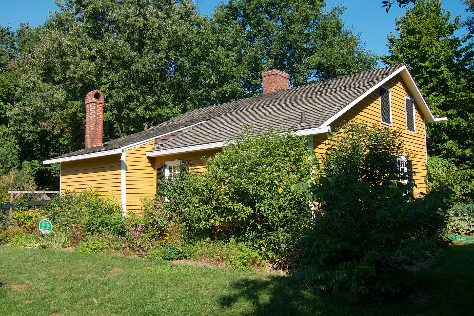 The yellow clapboard Bradley House at Bradley Museum in Mississauga, surrounded by gardens and tall trees