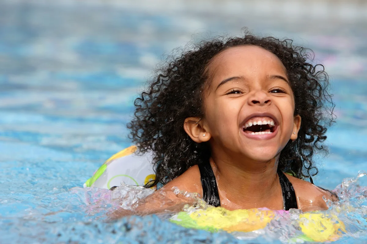 A smiling child splashing in a swimming pool with a flotation ring