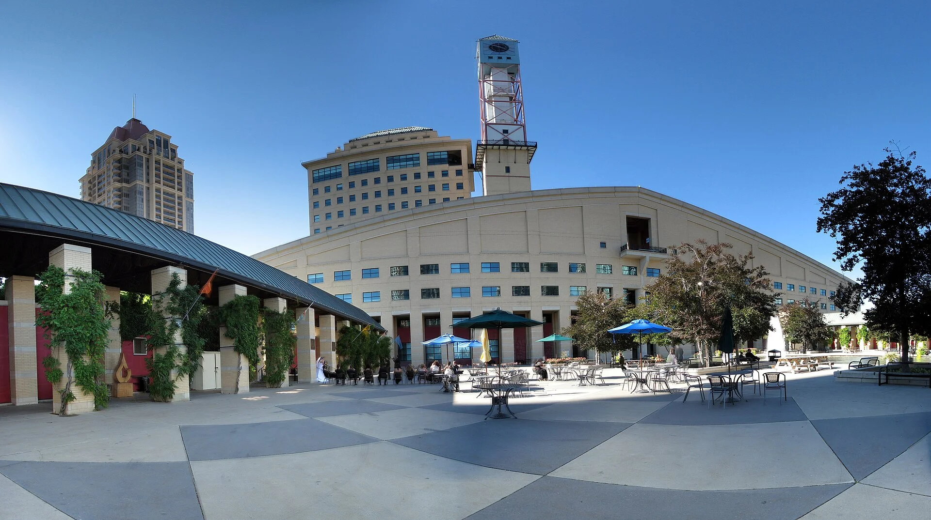 The Mississauga Civic Centre and its clock tower, seen across a public square with patio umbrellas on a sunny day