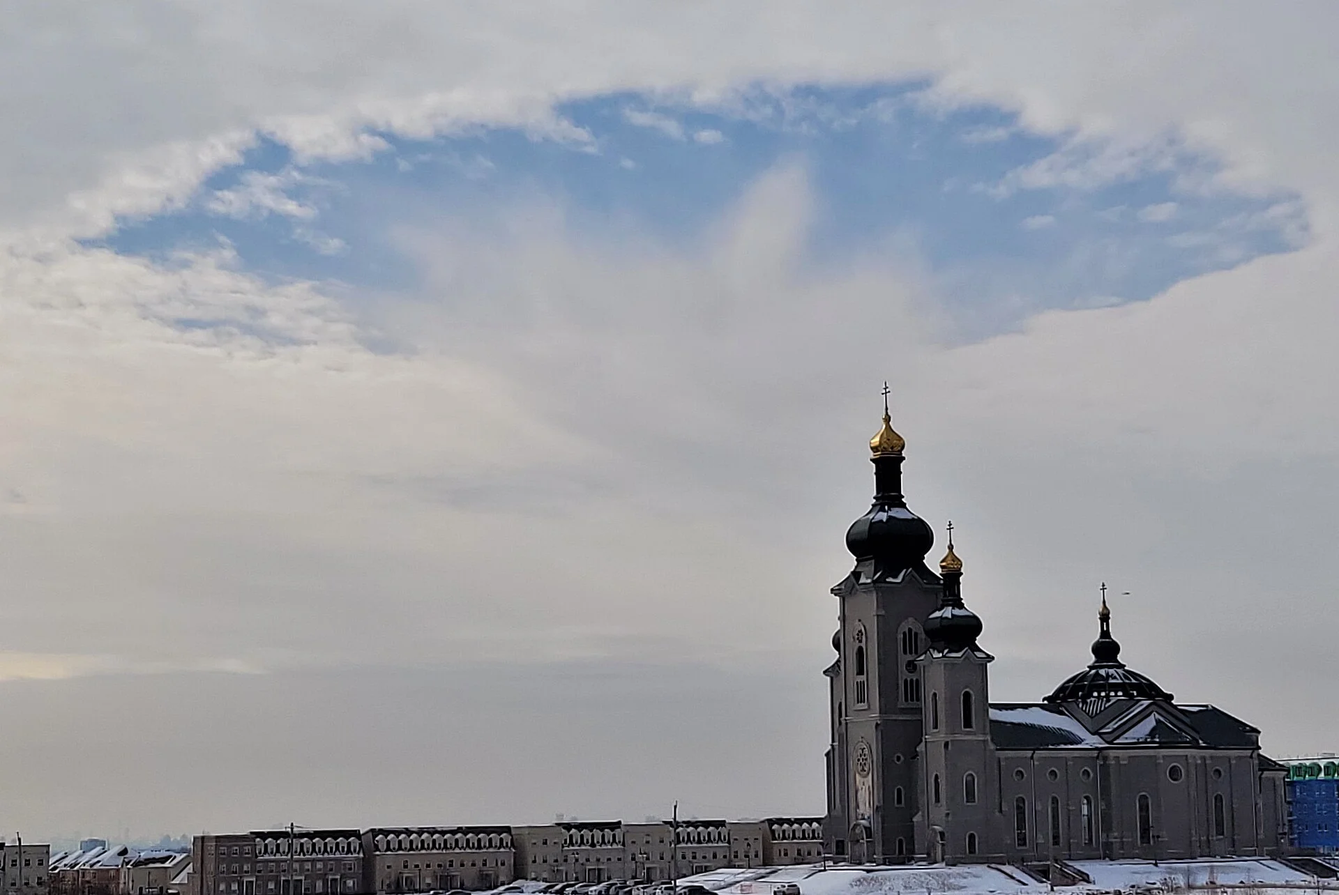 The gold-topped domes of the Cathedral of the Transfiguration in Markham under a cloudy winter sky, with snow on the ground