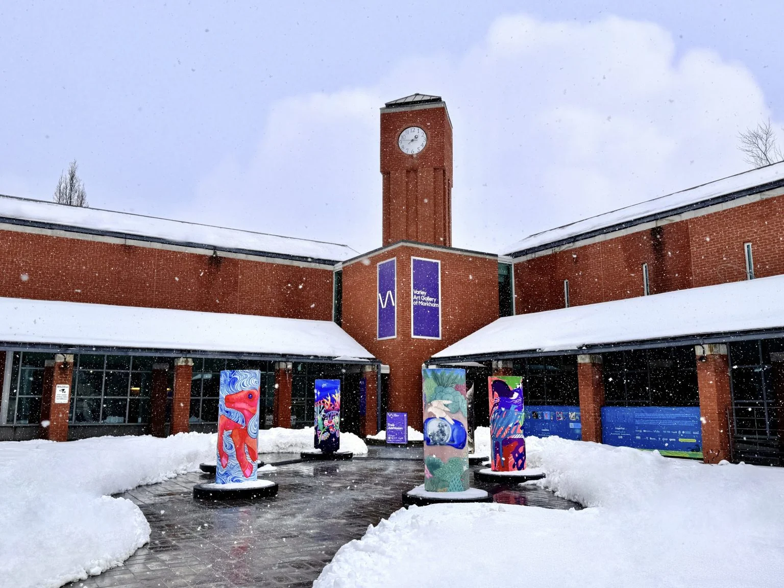 Tall painted lantern columns stand in the snowy courtyard of the Varley Art Gallery, below its brick clock tower