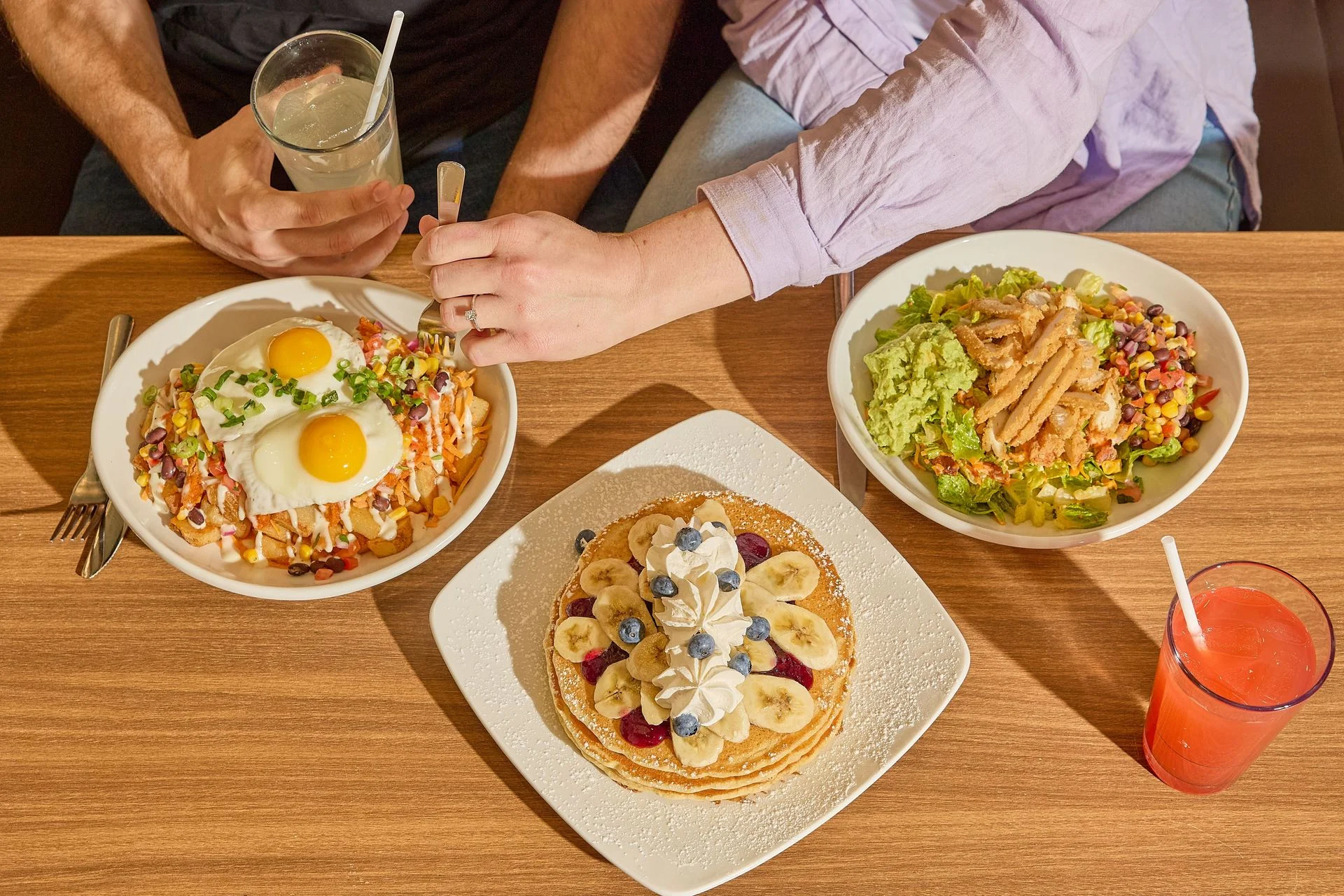 Pancakes topped with bananas and blueberries, eggs and a salad on a restaurant table