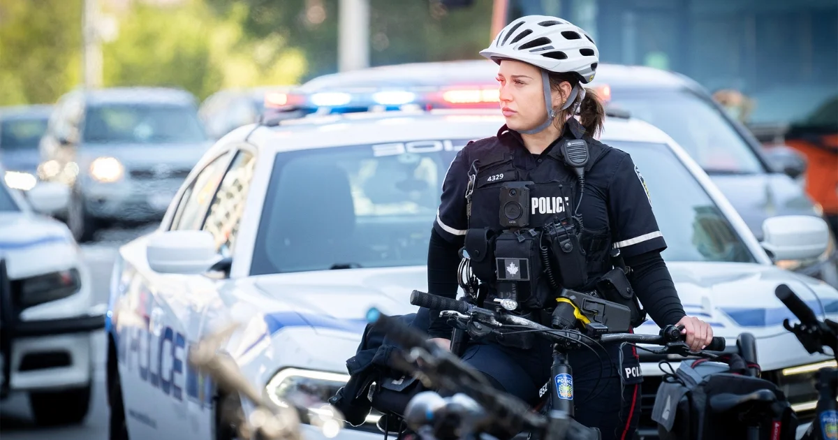 A Peel Regional Police bicycle officer stands beside marked police cruisers