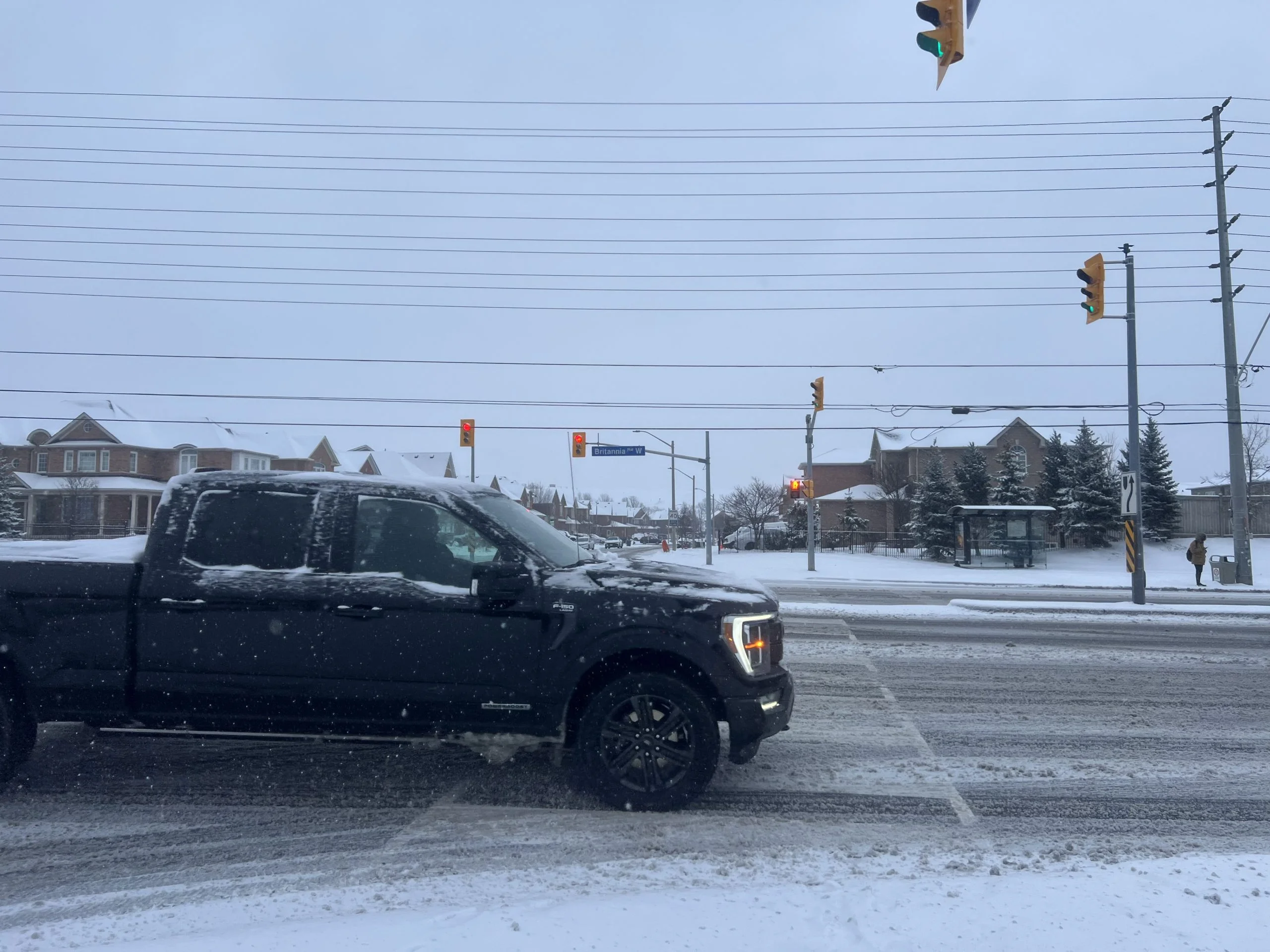A pickup truck drives through fresh snow at a suburban Mississauga intersection