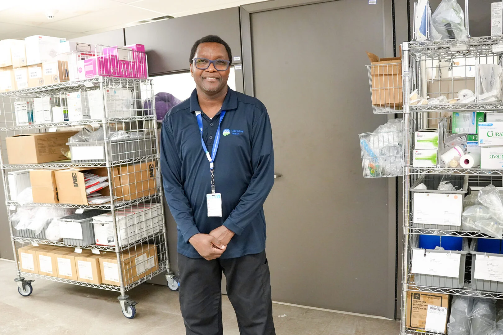 Paul Husbands stands between shelves of stocked supplies in a hospital supply room