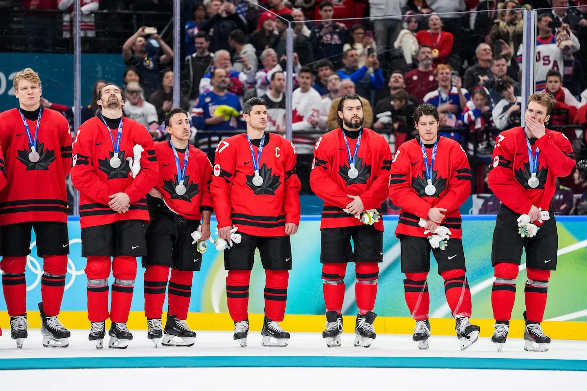 Canadian men's hockey players line up on the ice wearing silver medals after the Olympic final in Milan