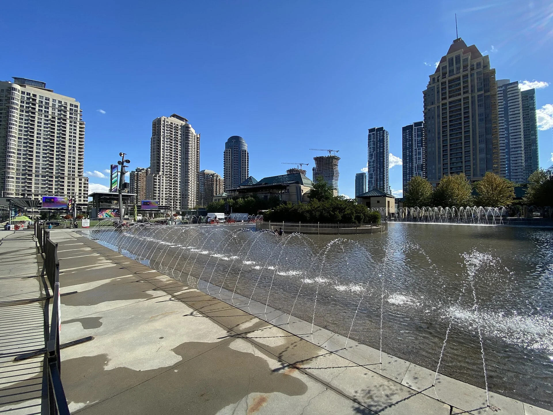 Mississauga Celebration Square with its fountain, outdoor screens and stage, surrounded by downtown condo towers on a sunny day