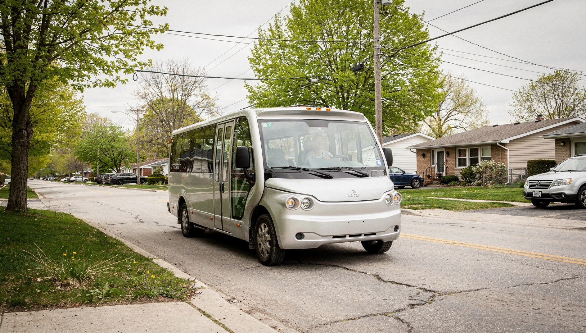 An electric minibus on a suburban street with fresh spring foliage.