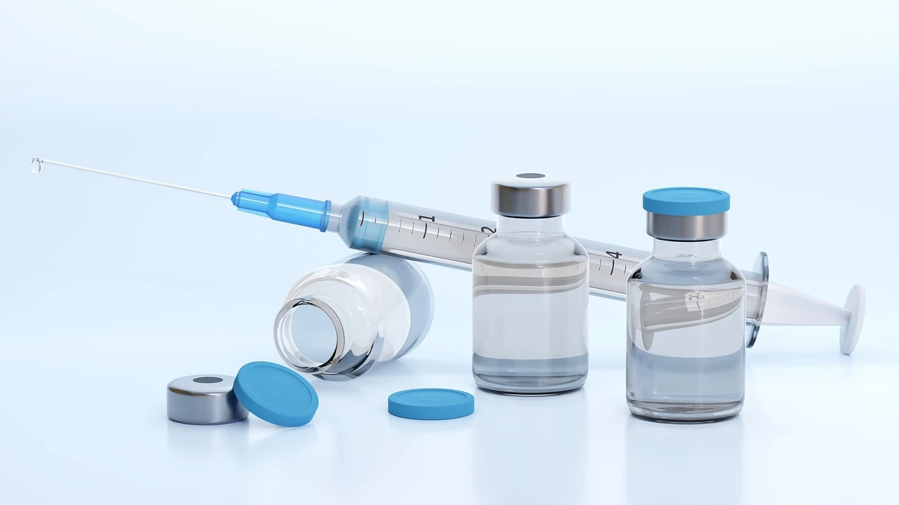 A gloved hand prepares a vaccine syringe from a vial on a clinic tray.