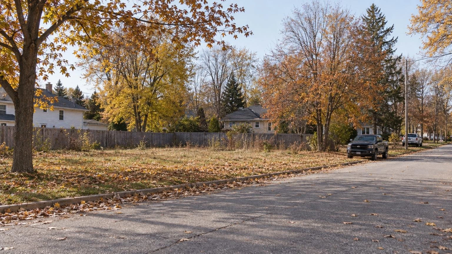 A vacant residential lot on a suburban street in Pelham, Ontario, surrounded by autumn trees.