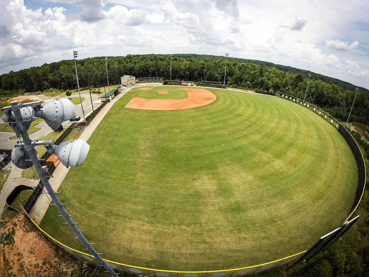 An empty community baseball field with a backstop and dugout under autumn trees.