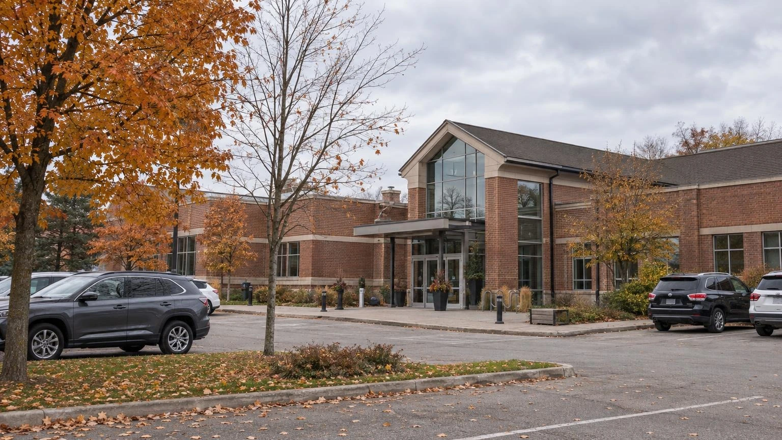 An Ontario municipal city hall building on an overcast autumn day, with a partly bare tree and parked cars in the foreground.