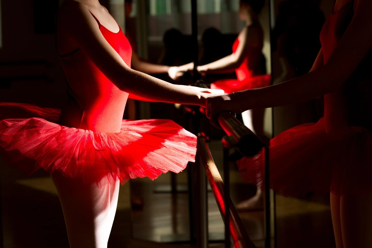 An empty dance studio with a wooden barre and large windows in autumn light.