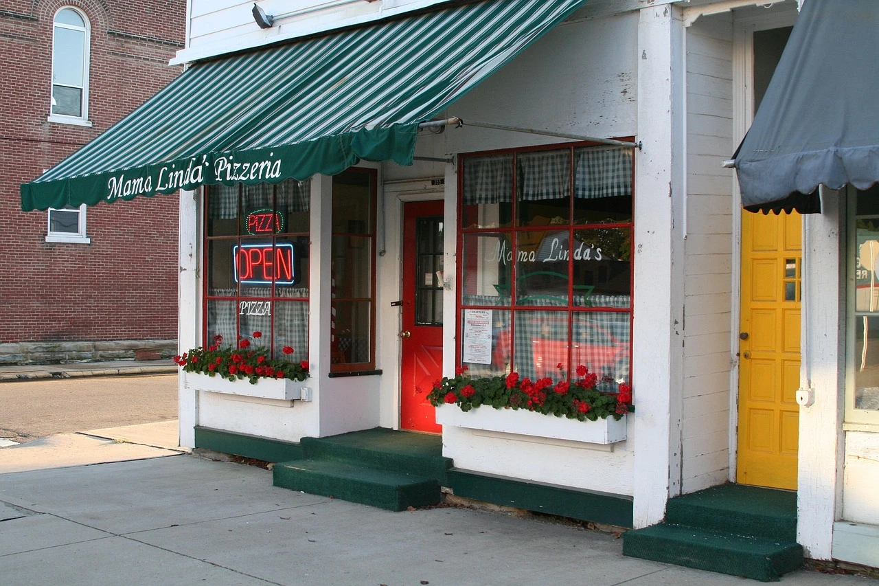 Small storefronts on an Ontario street with fallen autumn leaves and parked cars