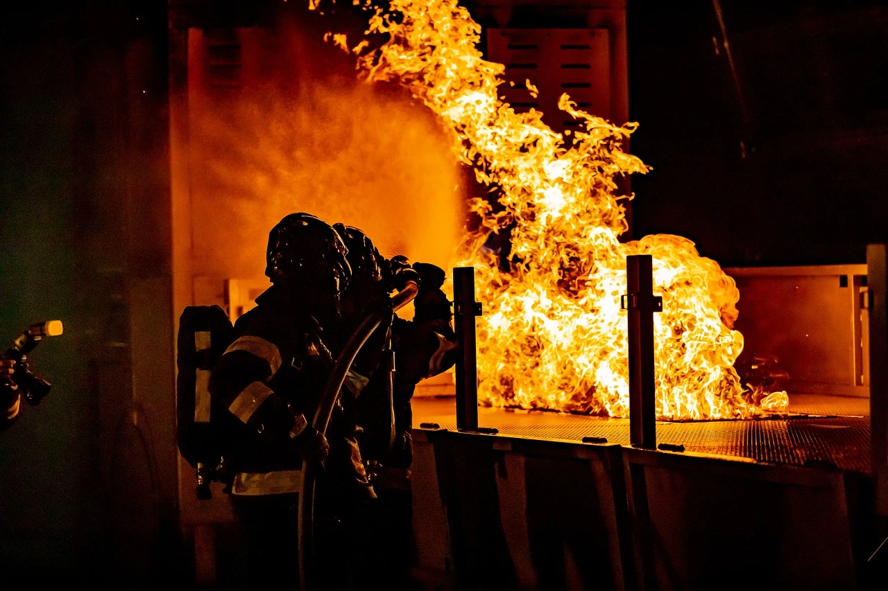 Illustration of firefighters working on a smoking roof at the rear of a small Ontario grocery store plaza at dusk