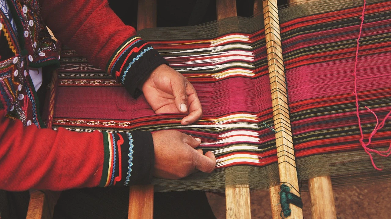 A hand loom, woven samples and fibre materials on a craft table in a library setting.