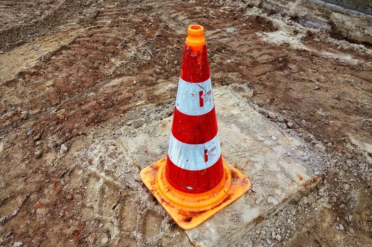 Road construction on a two-lane suburban street, with cones closing one lane and an excavator at work.