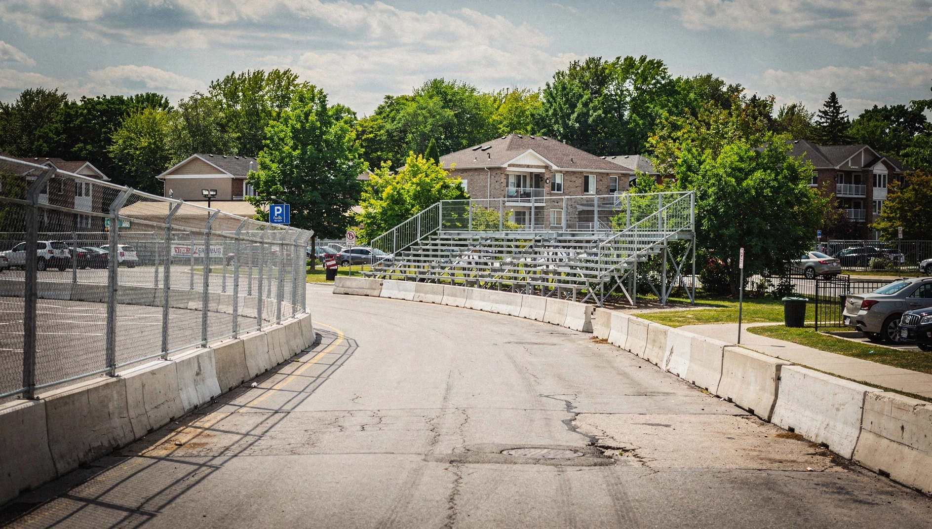 Illustration of a temporary street-racing circuit with safety fencing and grandstands in a suburban summer setting.