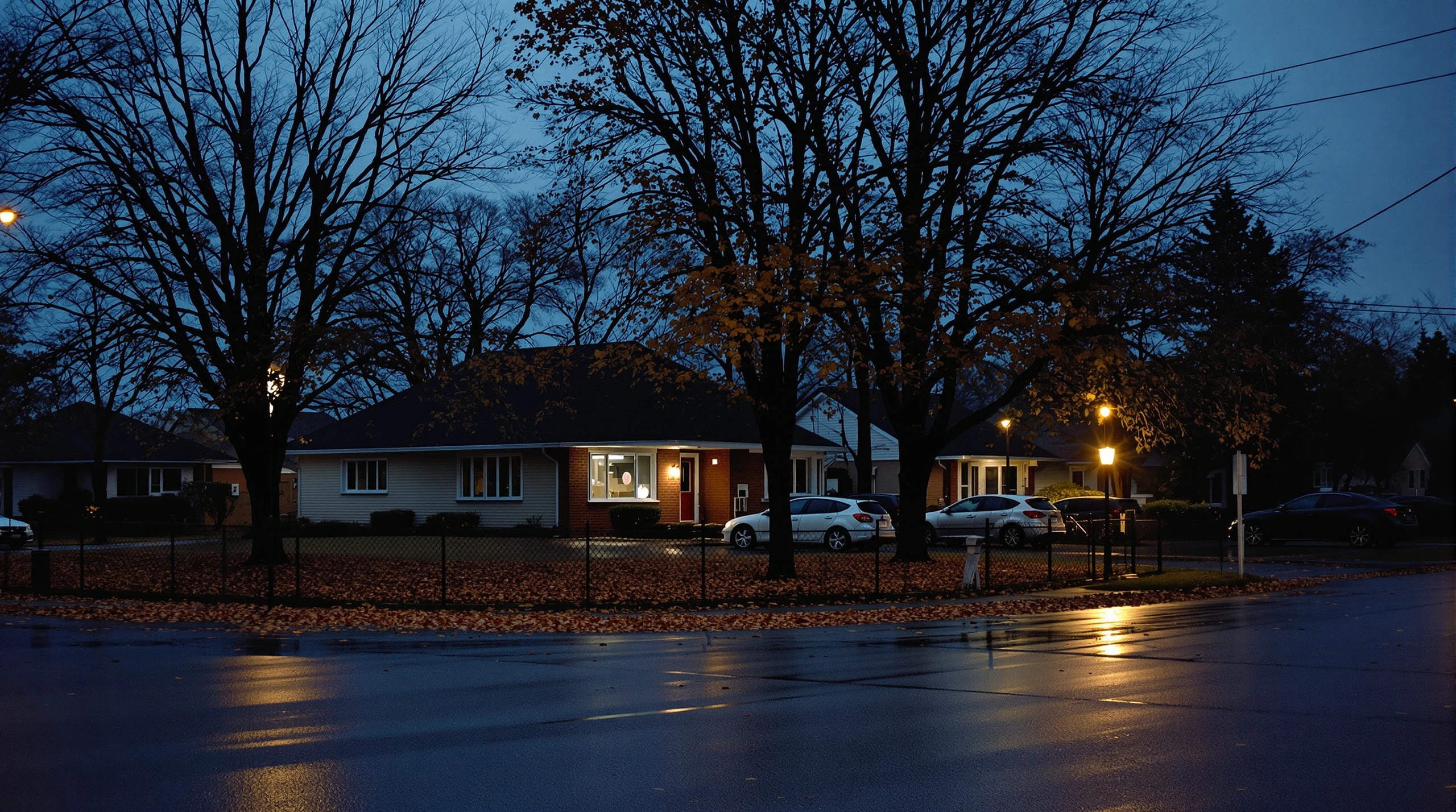 A quiet residential street in a small Ontario city at dusk, with autumn trees, parked cars and streetlights.