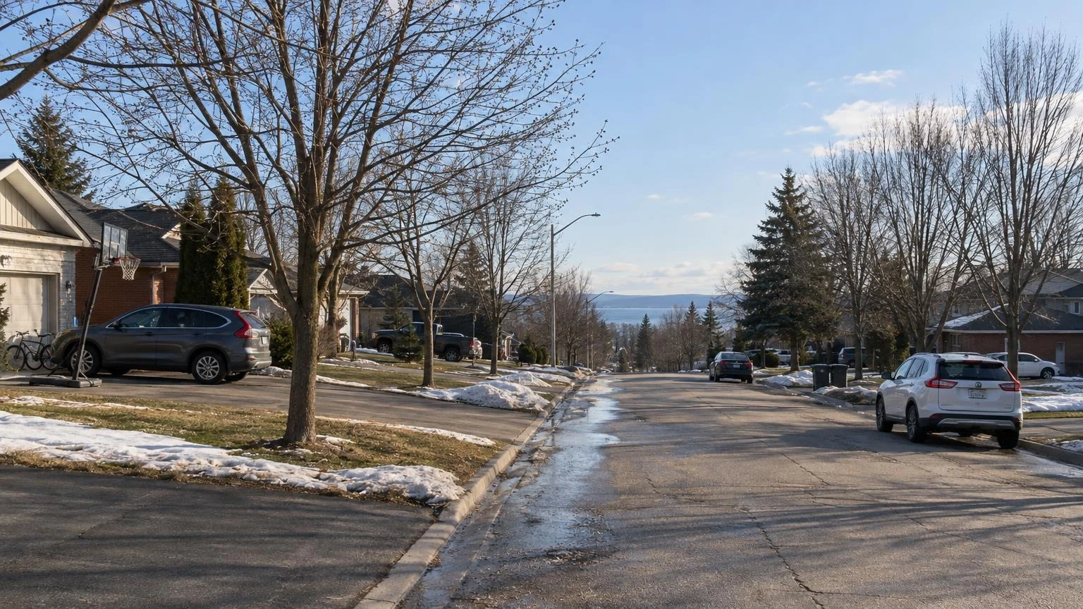 A residential street in Orillia on a sunny spring morning with budding trees and melting snow at the curbs.