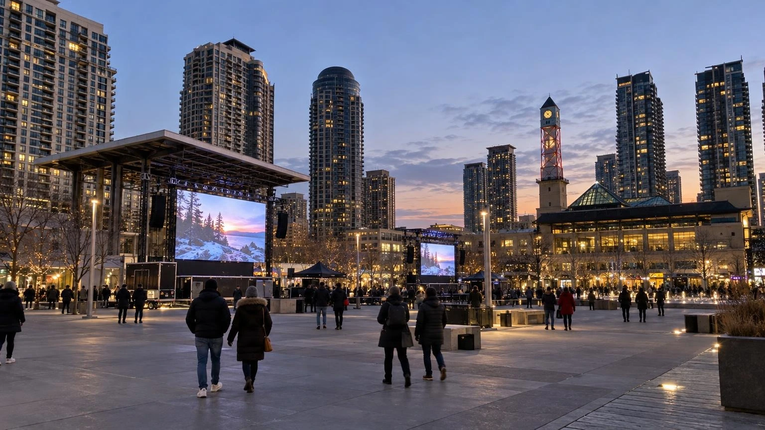 A wide shot of Celebration Square in Mississauga at dusk, with large outdoor screens and a gathering of people in a public plaza.