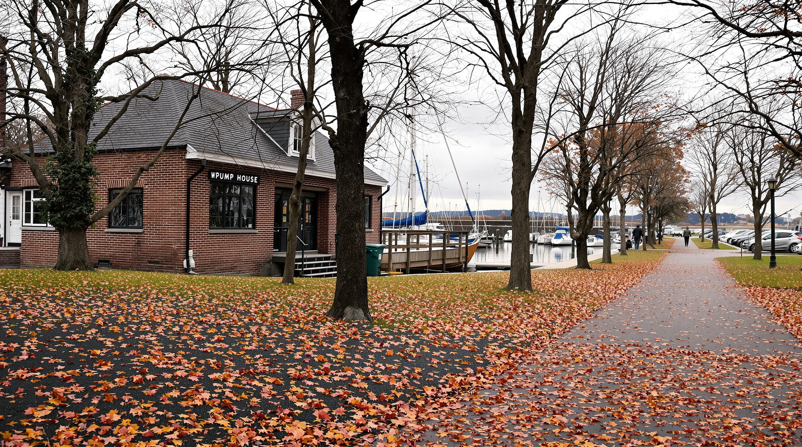 A heritage brick building beside a small harbour in Whitby on an overcast autumn day, with sailboats and fallen leaves along the waterfront.