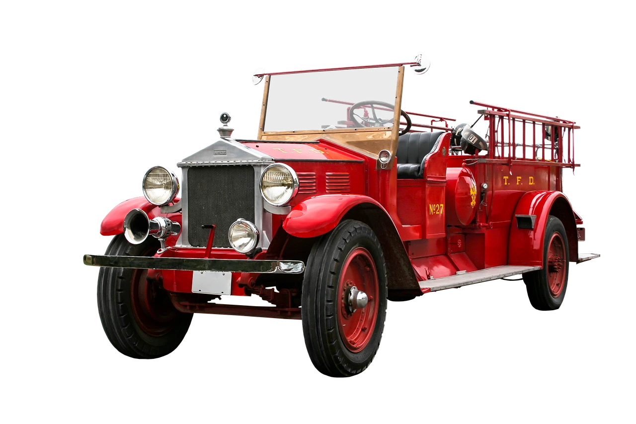 A red fire ladder truck parked on the grass at a green suburban park on a sunny summer evening.