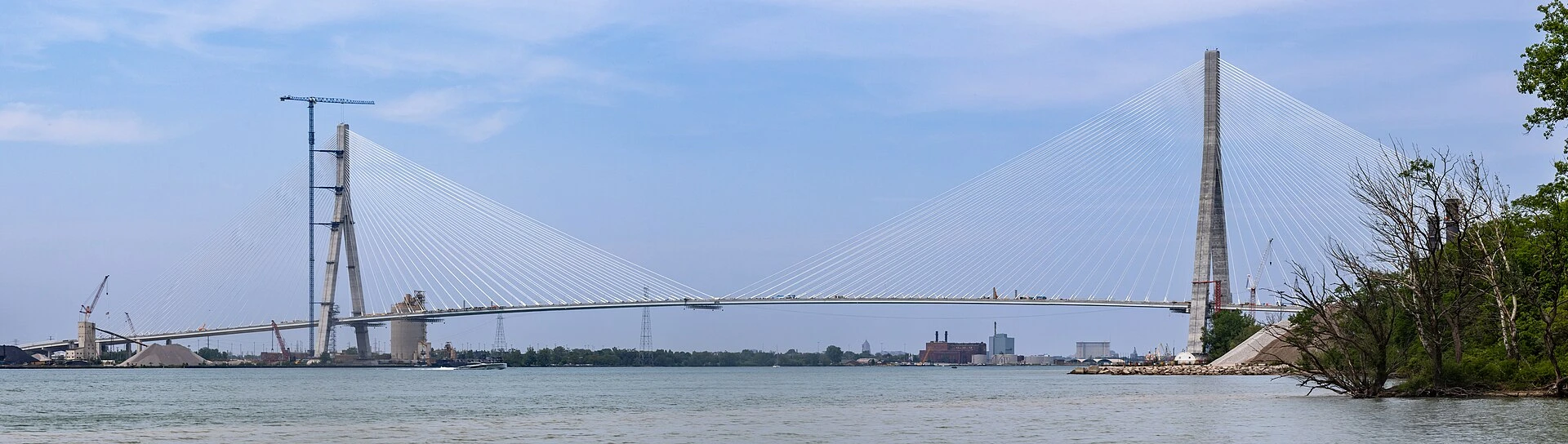 Illustration of a cable-stayed bridge spanning the Detroit River, viewed from the Windsor waterfront in summer.