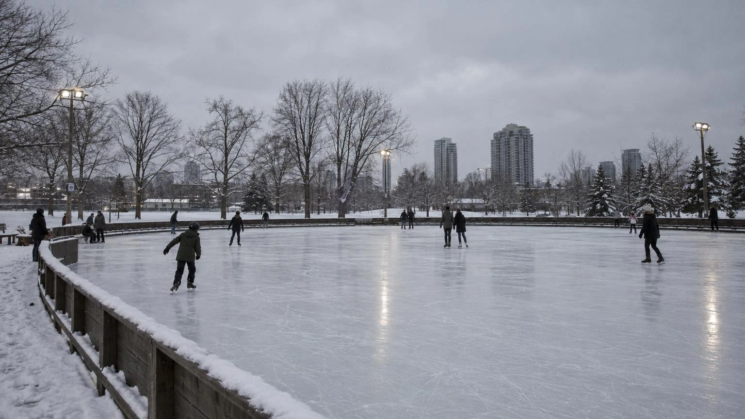 An outdoor ice skating rink covered in light snow under a cloudy winter sky.