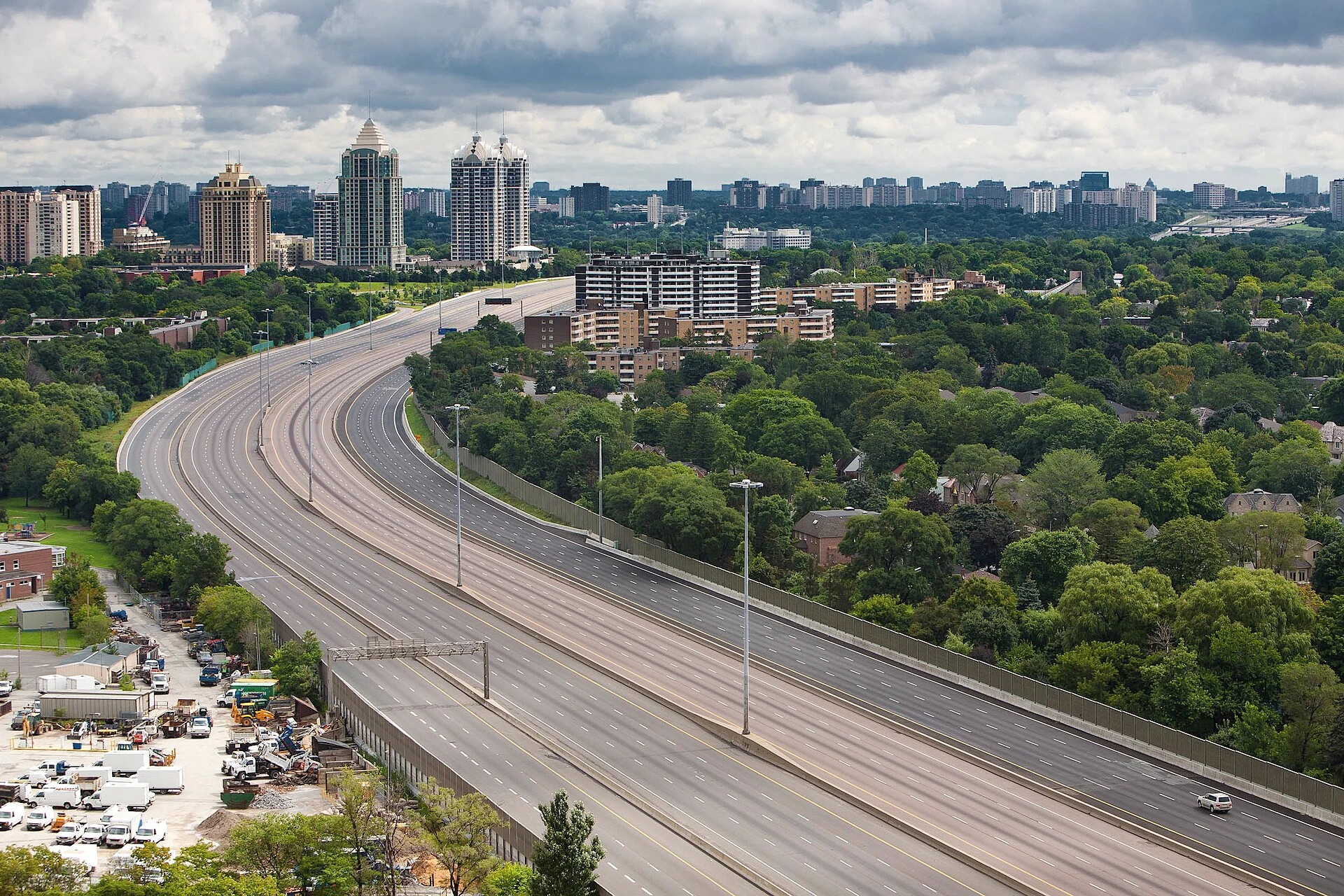 Illustration of traffic on a divided highway in Mississauga with concrete barriers and green summer foliage.