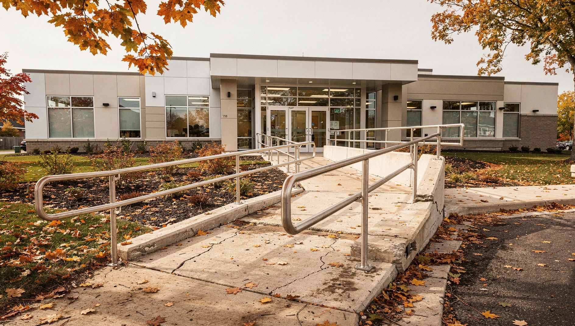 A bright, modern community centre entrance with a concrete ramp and metal handrails in Ontario during autumn.