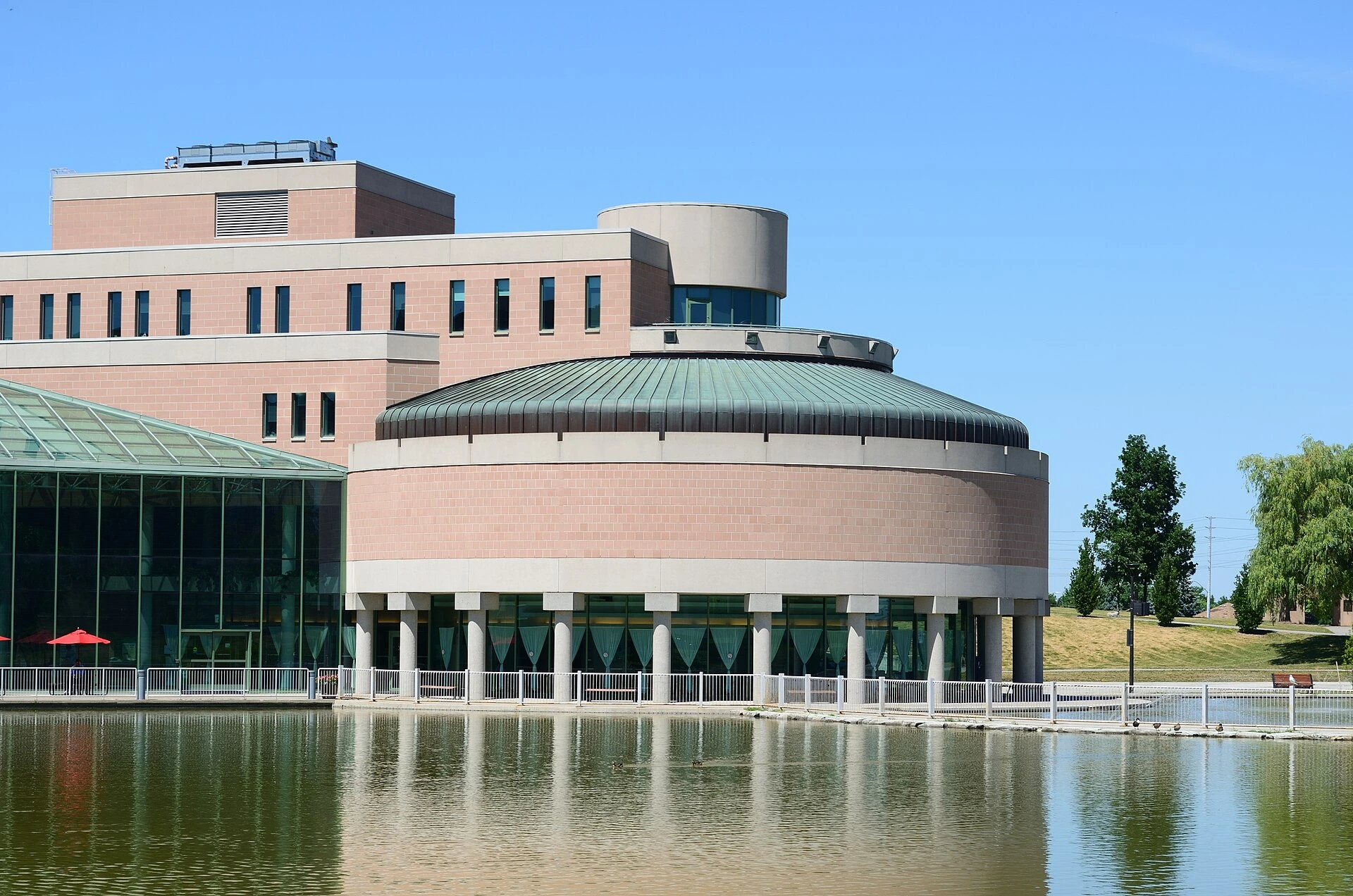 A modern civic building with large glass windows under a bright summer sky in a downtown urban setting.