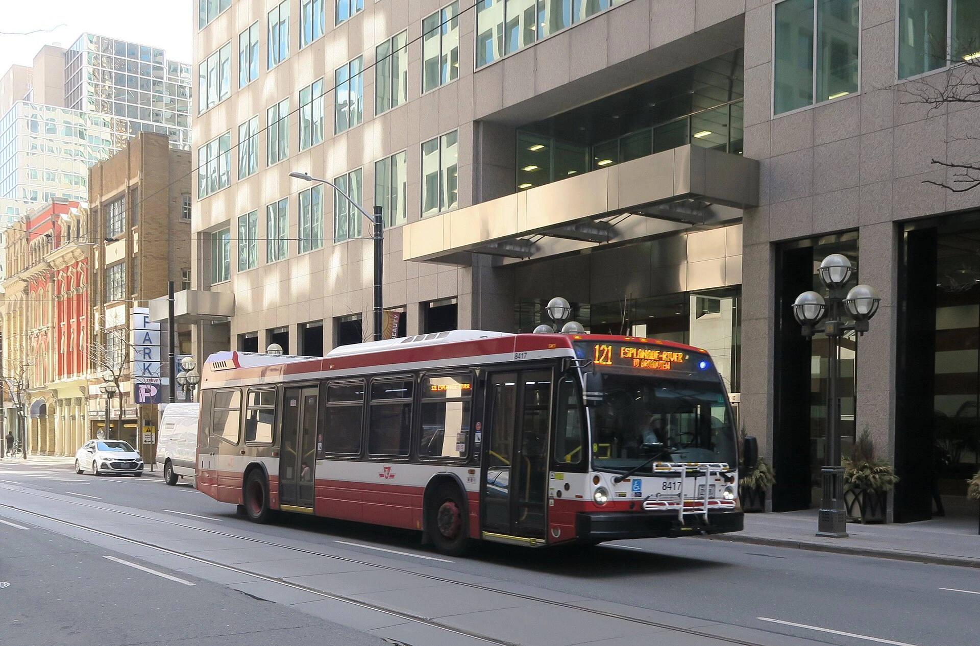 A Toronto transit bus driving past a subway station entrance during a cloudy autumn day.