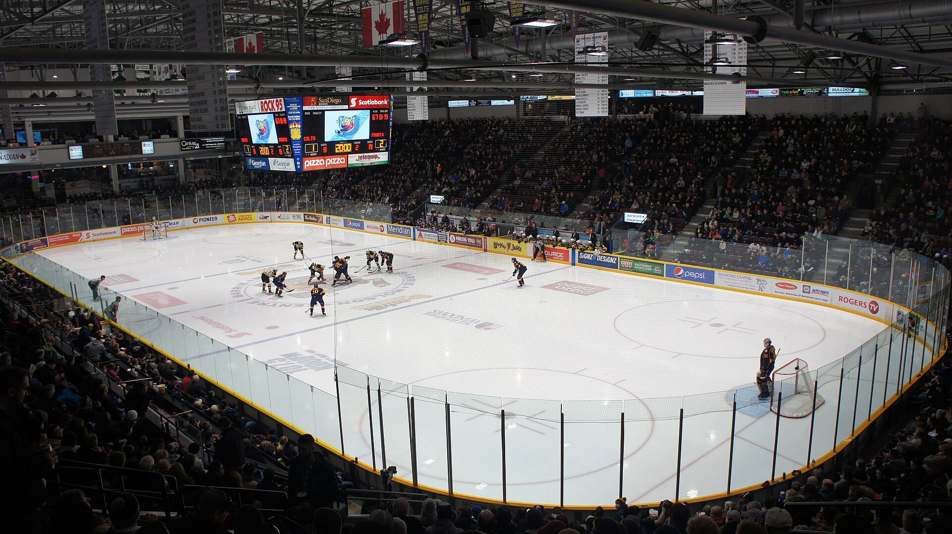 A junior hockey game in an arena, with a defenceman skating near the blue line and spectators in the stands behind.