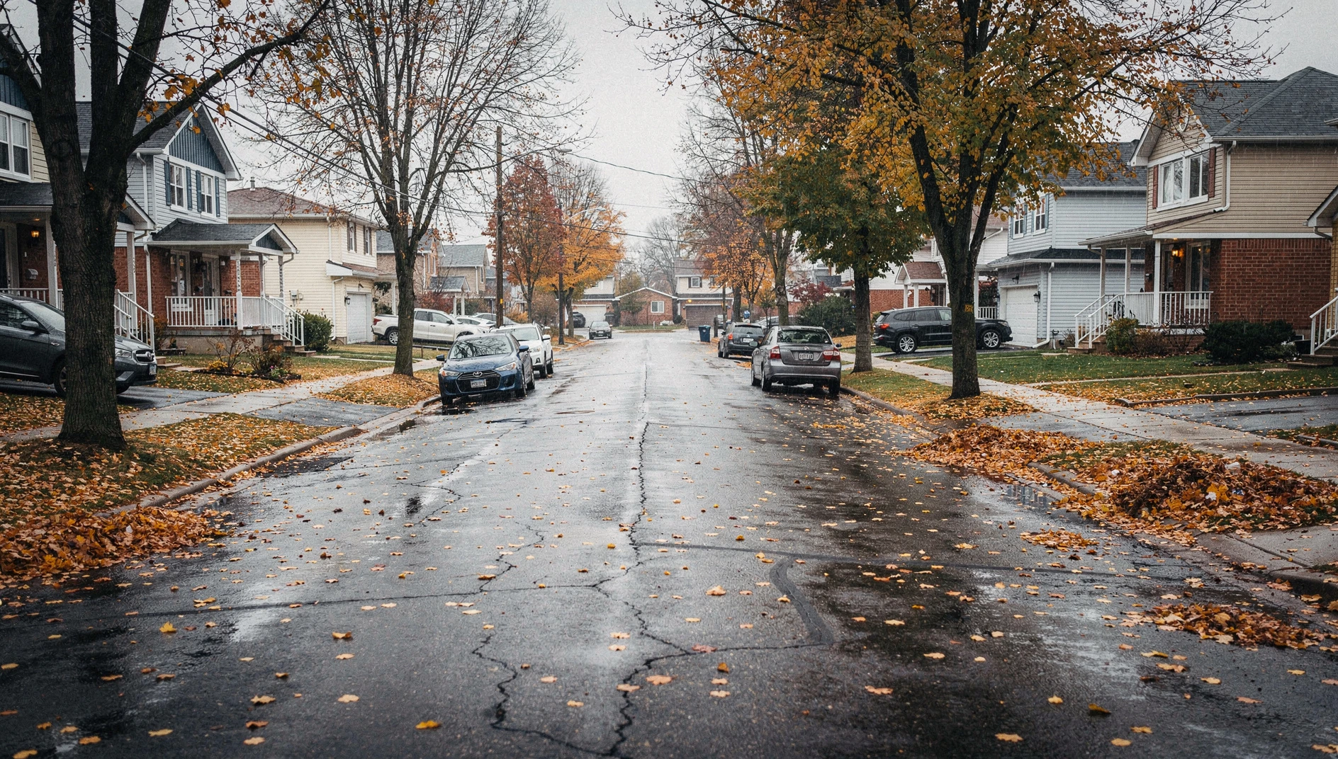 A wide shot of a suburban residential street in Ajax, Ontario, during a crisp autumn afternoon with fallen leaves on the pavement.