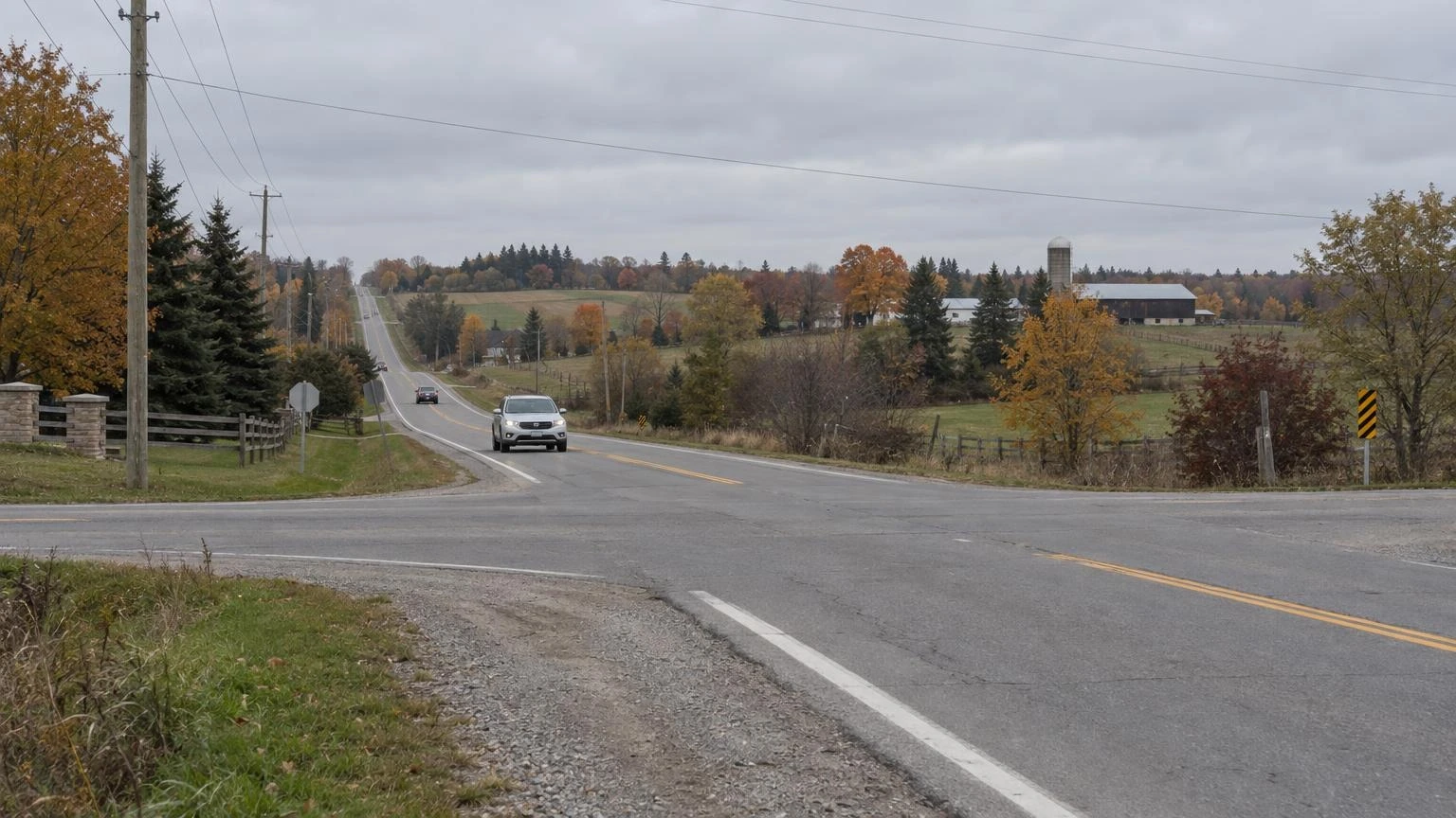 A quiet rural intersection in Caledon, Ontario, with green fields and a paved road under an autumn sky.
