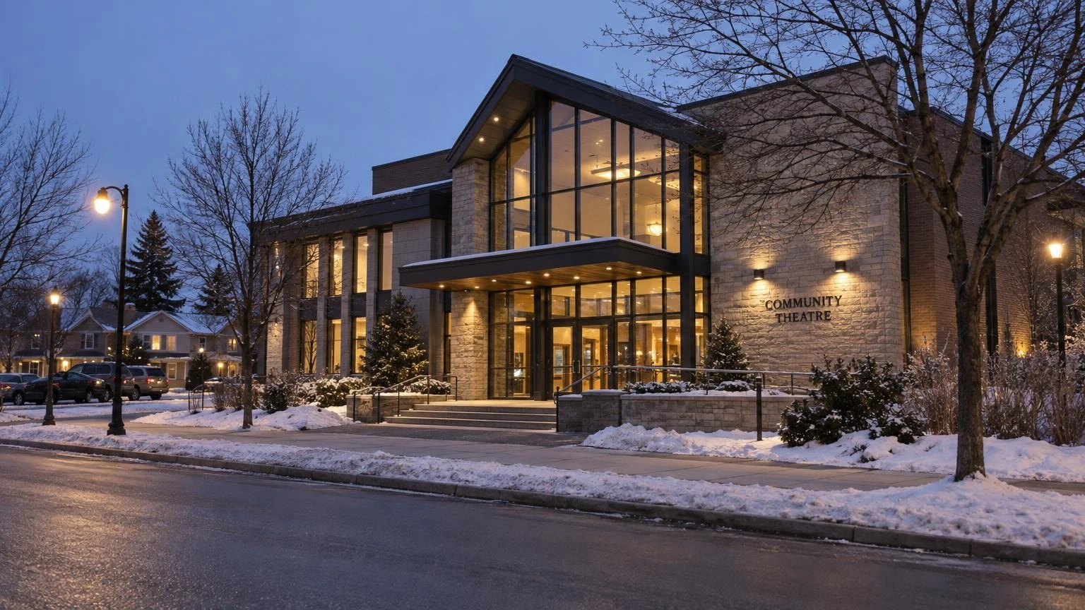 A wide shot of a modern community theatre entrance in Mississauga during a late winter evening, with soft interior lights visible through glass doors.