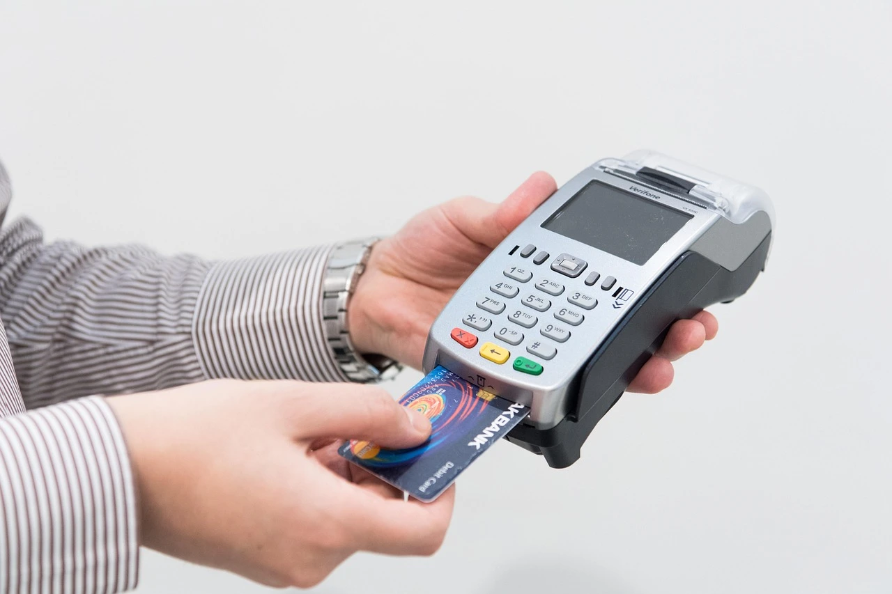 A hand inserts a debit card into a portable payment terminal on a city sidewalk, with a blurred taxi in the background.