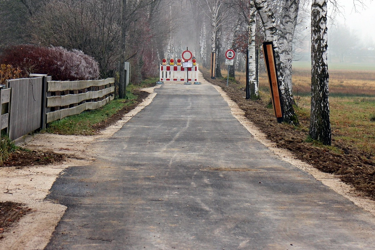 A rural two-lane road in Thorold, Ontario, with traffic cones and construction barricades where asphalt repair work is underway on an autumn morning.