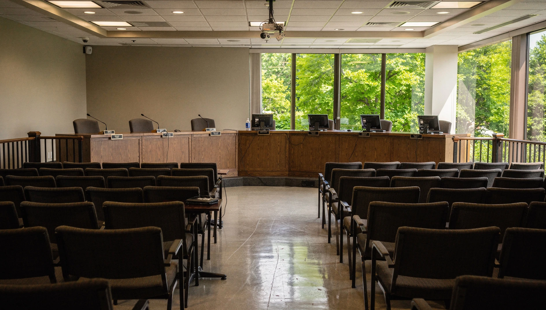 Illustration of an empty municipal council chamber with public seating and council desks.