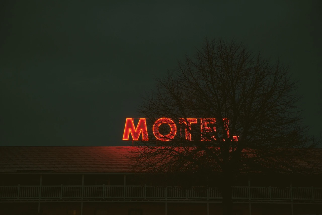 Illustrative view of a modest roadside motel exterior with a small parking area and autumn trees.