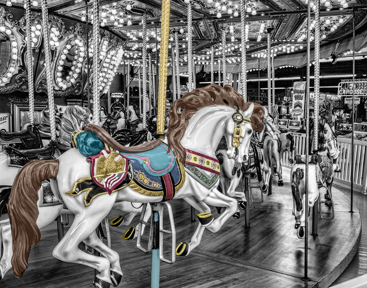 A vintage carousel surrounded by orange and gold autumn trees at a lakeside park, with the lake visible in the background.