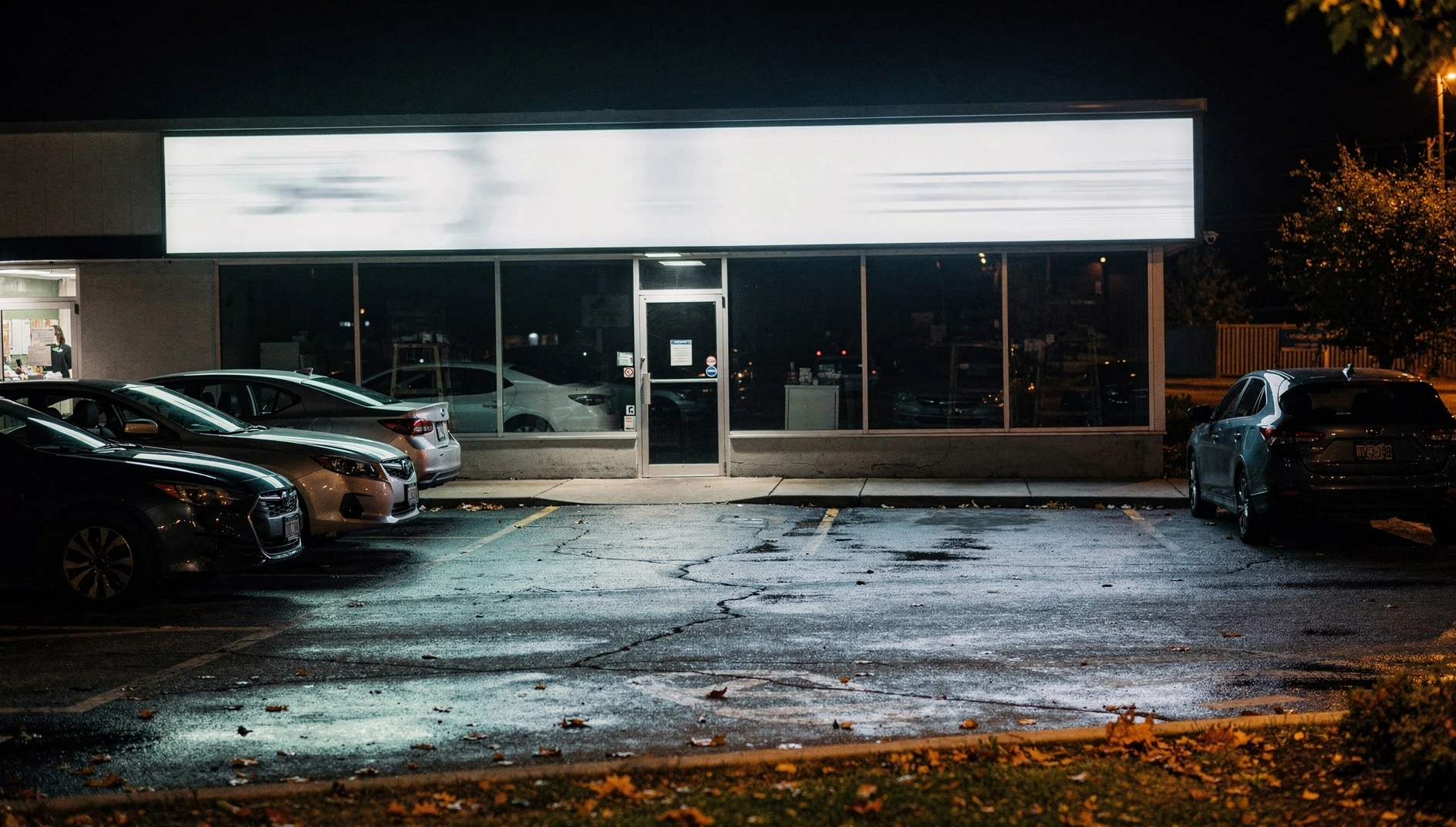 Illustration of a commercial storefront in a suburban plaza at night, with an empty parking lot.
