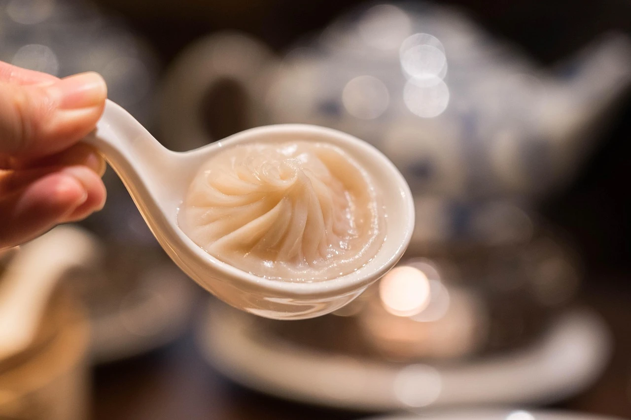 A table inside a casual Chinese restaurant with steaming baskets of dumplings and bowls of noodles.