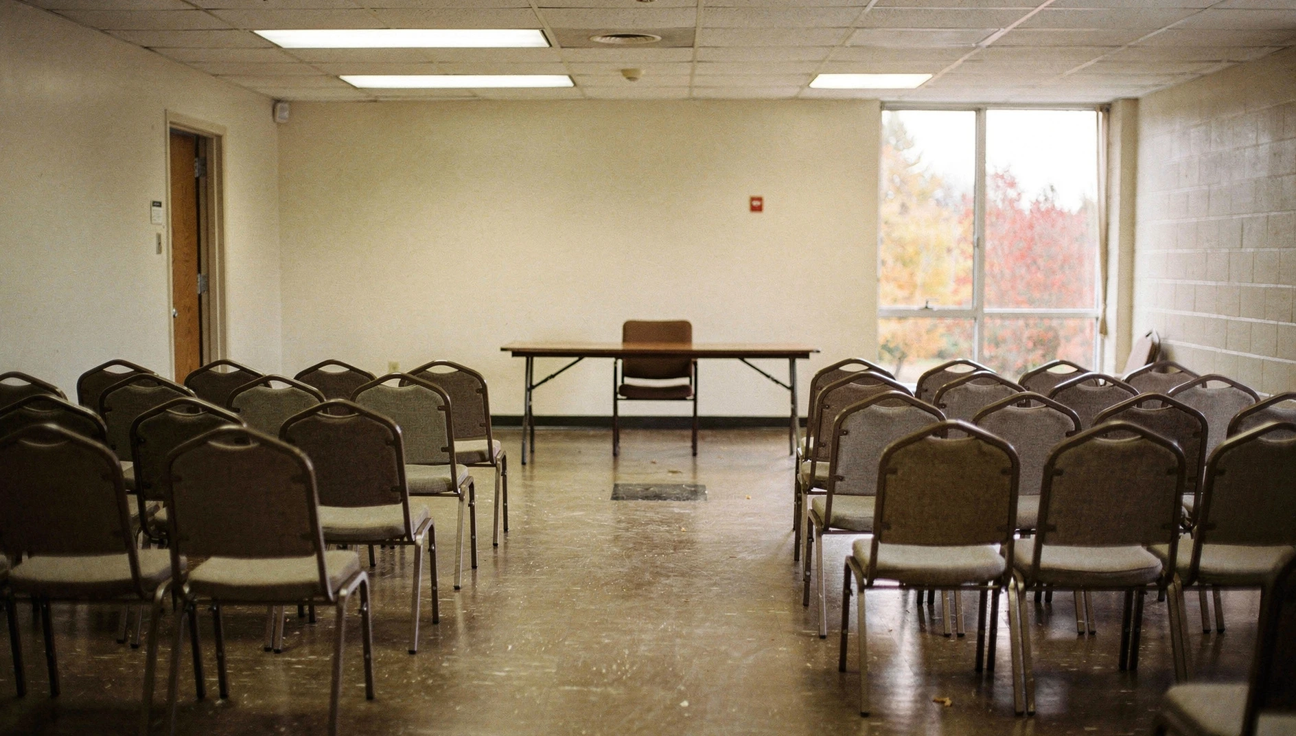 Rows of chairs facing a table in a community centre meeting hall.
