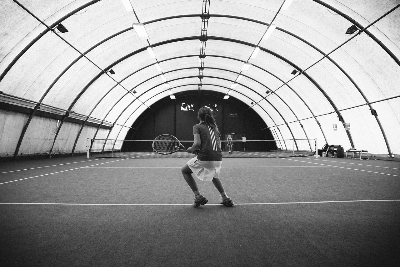 An empty indoor tennis court inside a community recreation complex, with a net stretched across the court surface.