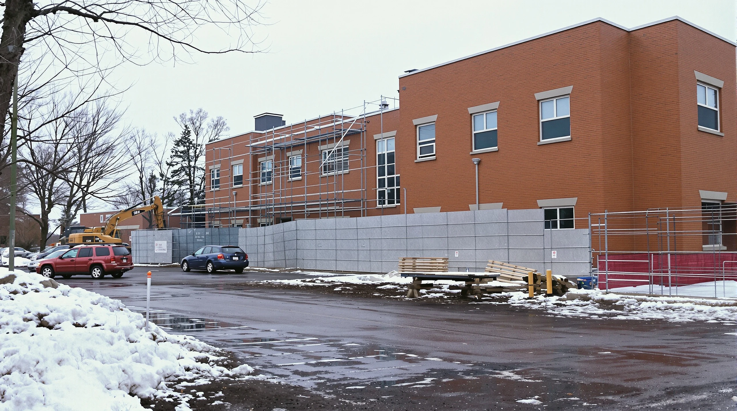 Construction equipment beside an existing hospital building on a snowy late-winter day