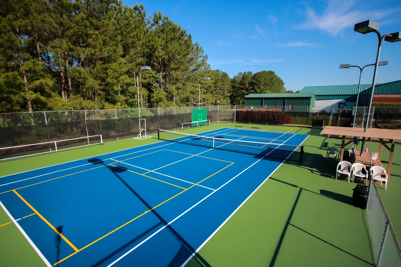 An outdoor pickleball court with distant players and green trees in summer.